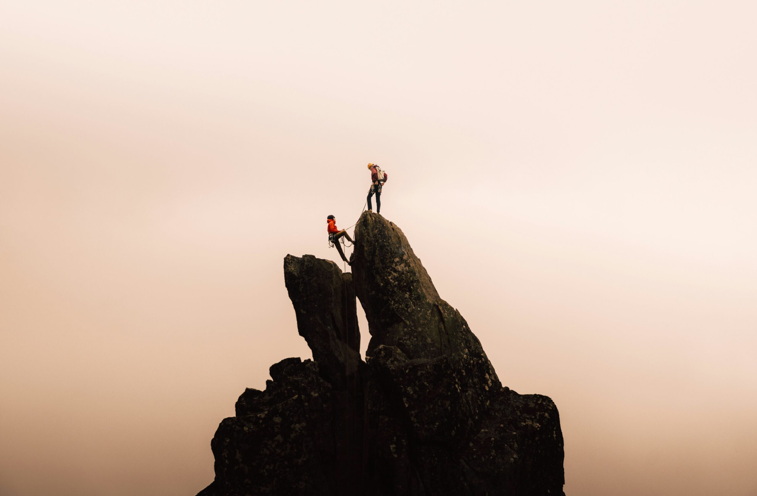 Smiling climber holding her favorite belay device atop a cliff
